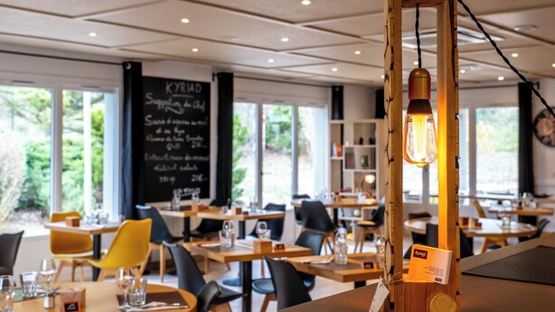 A restaurant interior with wooden tables, black chairs, and a hanging light fixture. - Kyriad Digne les Bains (Digne-les-Bains)