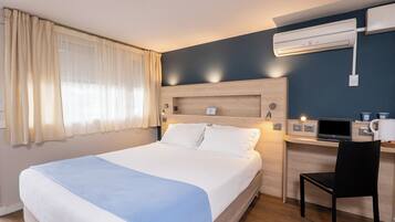 Hotelkamer met een bed, een bureau, een stoel, een airconditioner en een raam met gordijnen.