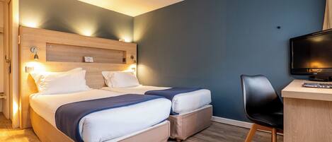 Habitación de hotel con dos camas, un escritorio con silla y una televisión.