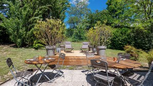 An outdoor patio with a wooden table and chairs, surrounded by lush greenery and trees. - Kyriad Digne les Bains (Digne-les-Bains)