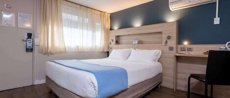 Una habitación de hotel con una cama, un escritorio y un equipo de aire acondicionado.