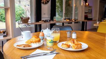 A breakfast table with croissants, a coffee cup, a teapot, a jug of orange juice, and salt and pepper shakers.