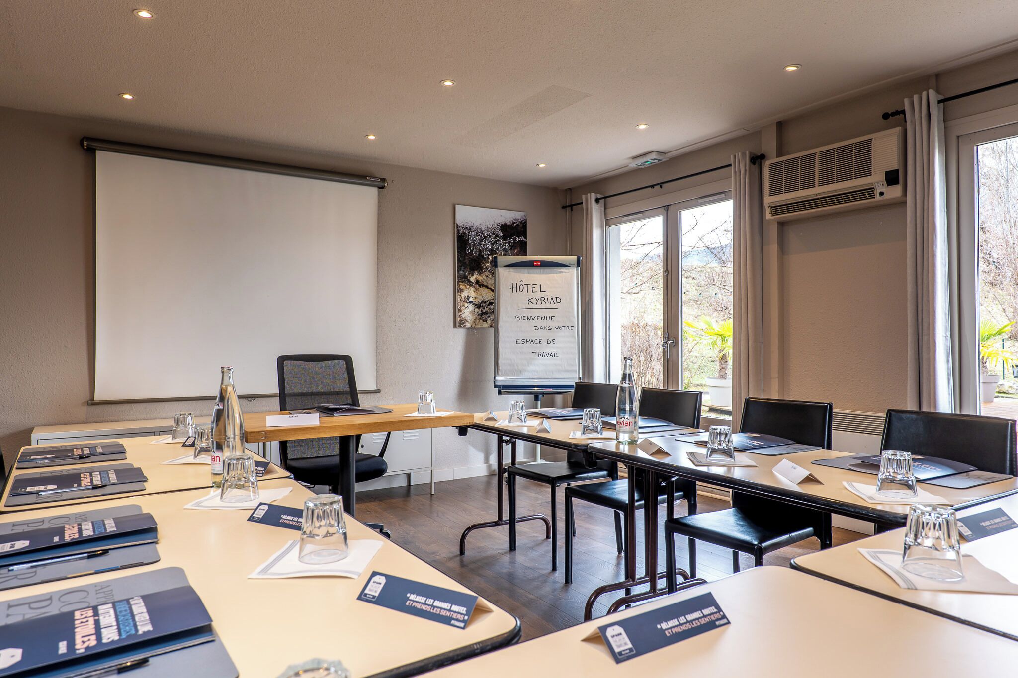 A conference room with tables, chairs, a projector screen, and a whiteboard.