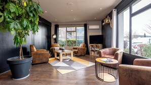 A modern living room with a large potted plant, leather armchairs, a coffee table, and a bookshelf. - Kyriad Digne les Bains (Digne-les-Bains)