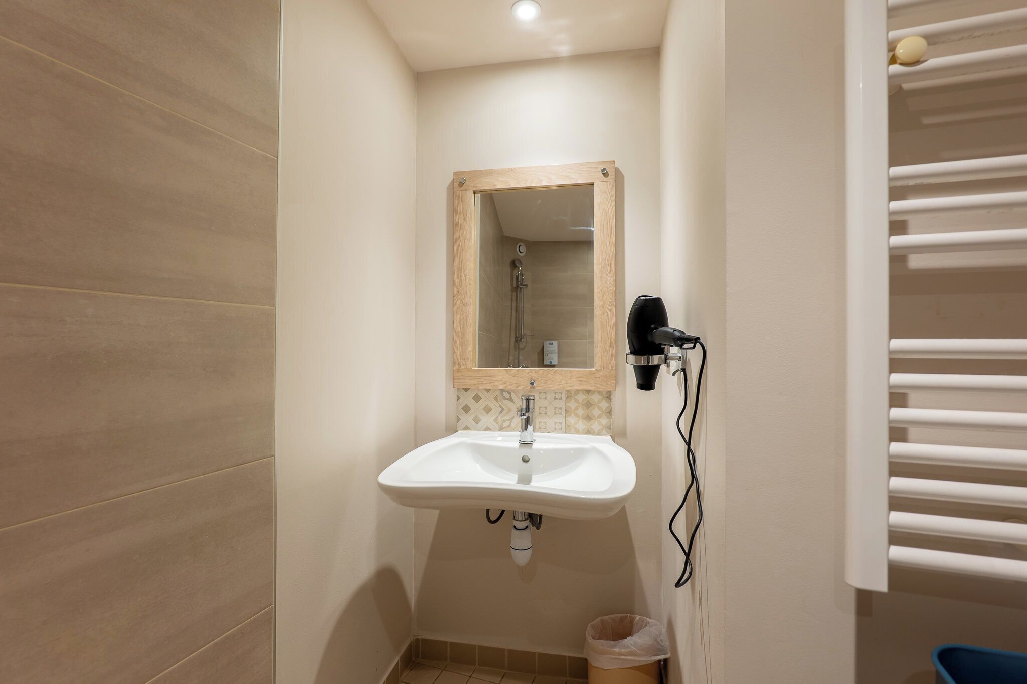 Un baño pequeño con lavamanos blanco, un espejo y ducha.