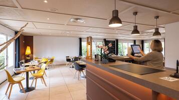 A modern hotel lobby with a reception desk, yellow chairs, and a large window offering a view of the outdoors.