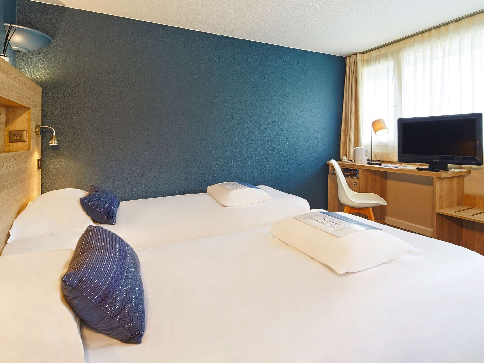 Une chambre d’hôtel avec deux lits, un bureau avec une télévision et un espace douche.
