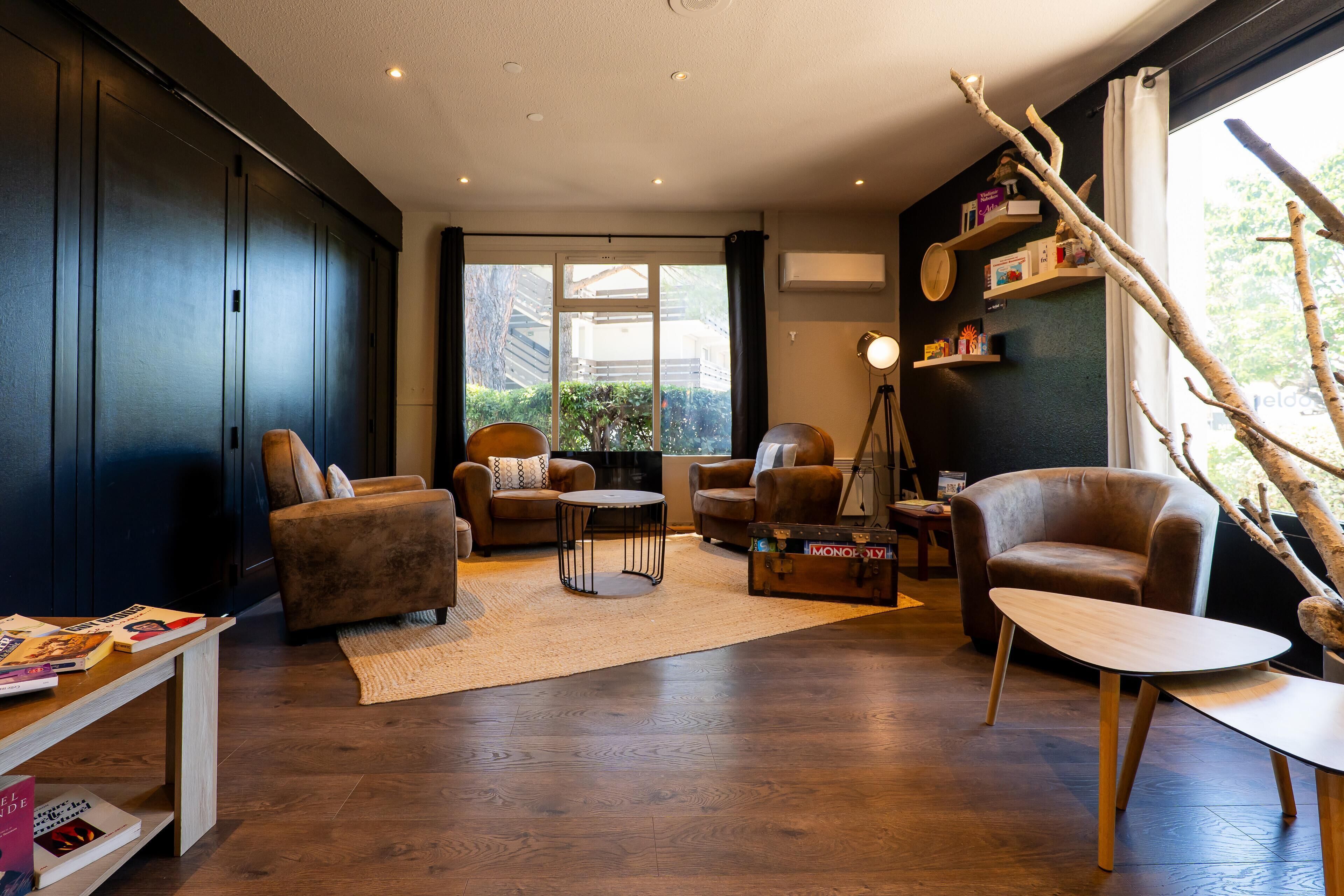 Una sala moderna con suelo de madera oscura, sofás de cuero, una mesa de centro y una estantería.