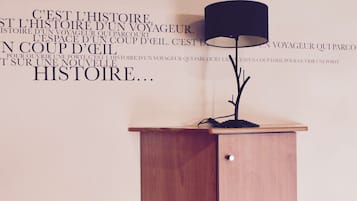 Una pared con un texto en francés sobre la historia de un viajero y una lámpara negra sobre un mueble de madera.