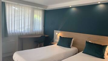 Habitación de hotel con dos camas, un escritorio y una ventana con cortinas de encaje.