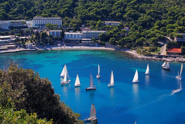 A coastal town with sailboats on a turquoise sea, surrounded by buildings and greenery. - Hotel Vis (Dubrovnik)