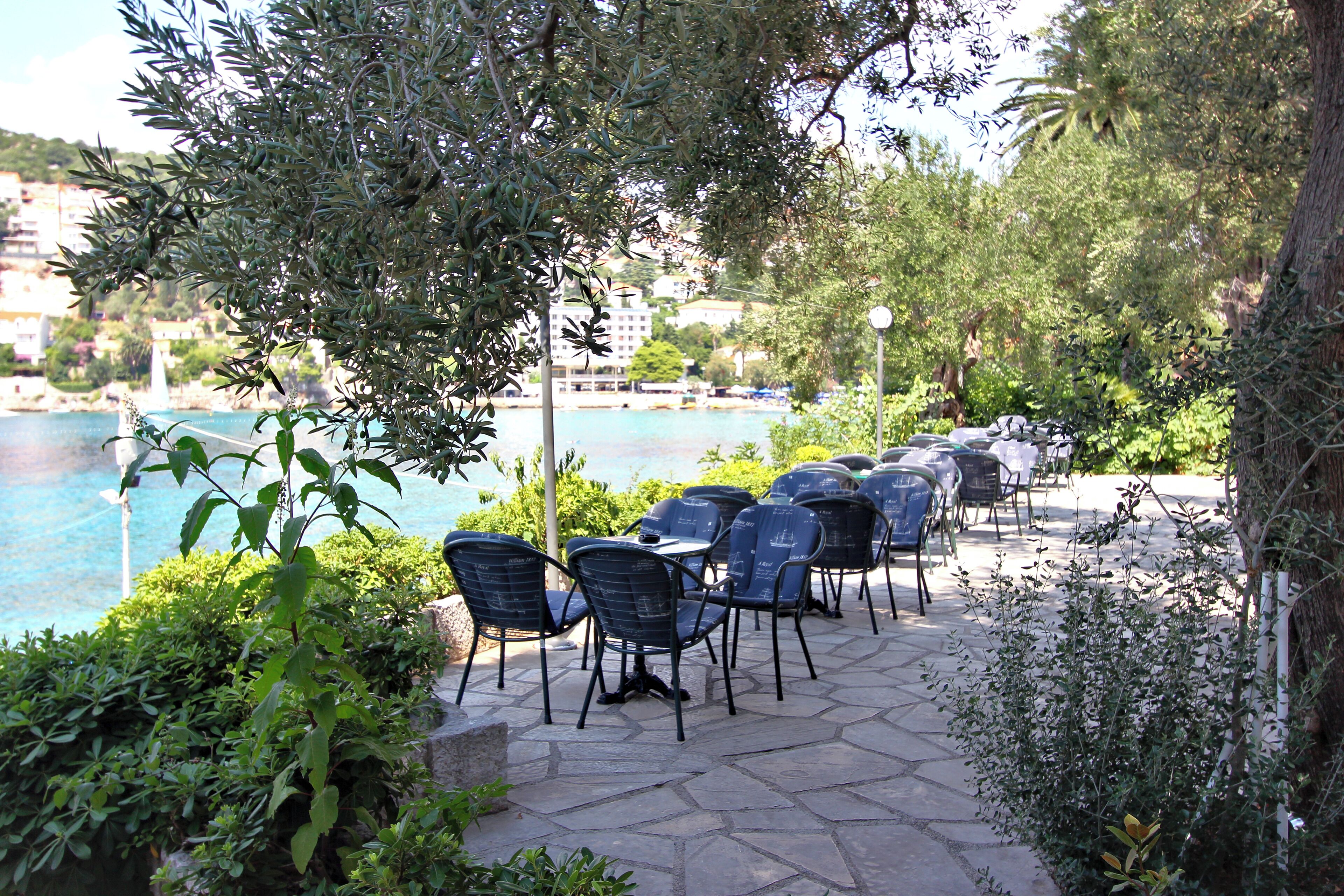 Un espace extérieur aménagé avec des tables et des chaises, offrant une vue sur un plan d’eau et sur le paysage urbain.