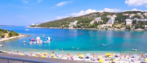 Una playa costera con aguas azul turquesa, una orilla arenosa y vistas a edificios en una ladera.