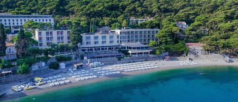 Un hôtel situé sur la côte, composé de plusieurs bâtiments, avec une plage équipée de transats et offrant une vue dégagée sur la mer.