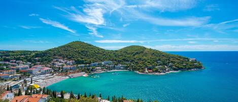 A coastal town with a clear blue sea, a small bay, and a hill with buildings.