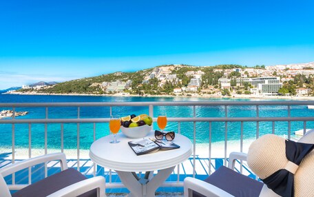 A balcony with a table set for two, overlooking a coastal town and the sea.