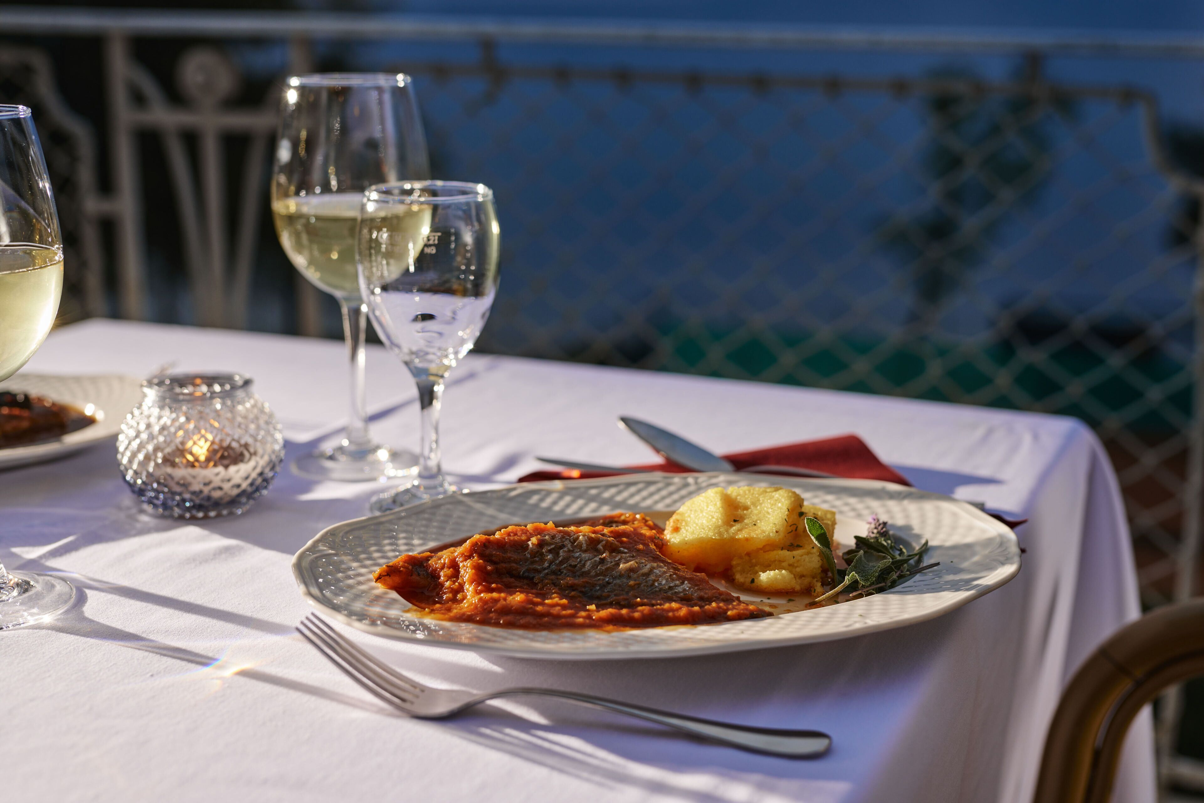 Une table à manger avec une assiette de nourriture, un verre de vin blanc et une bougie.