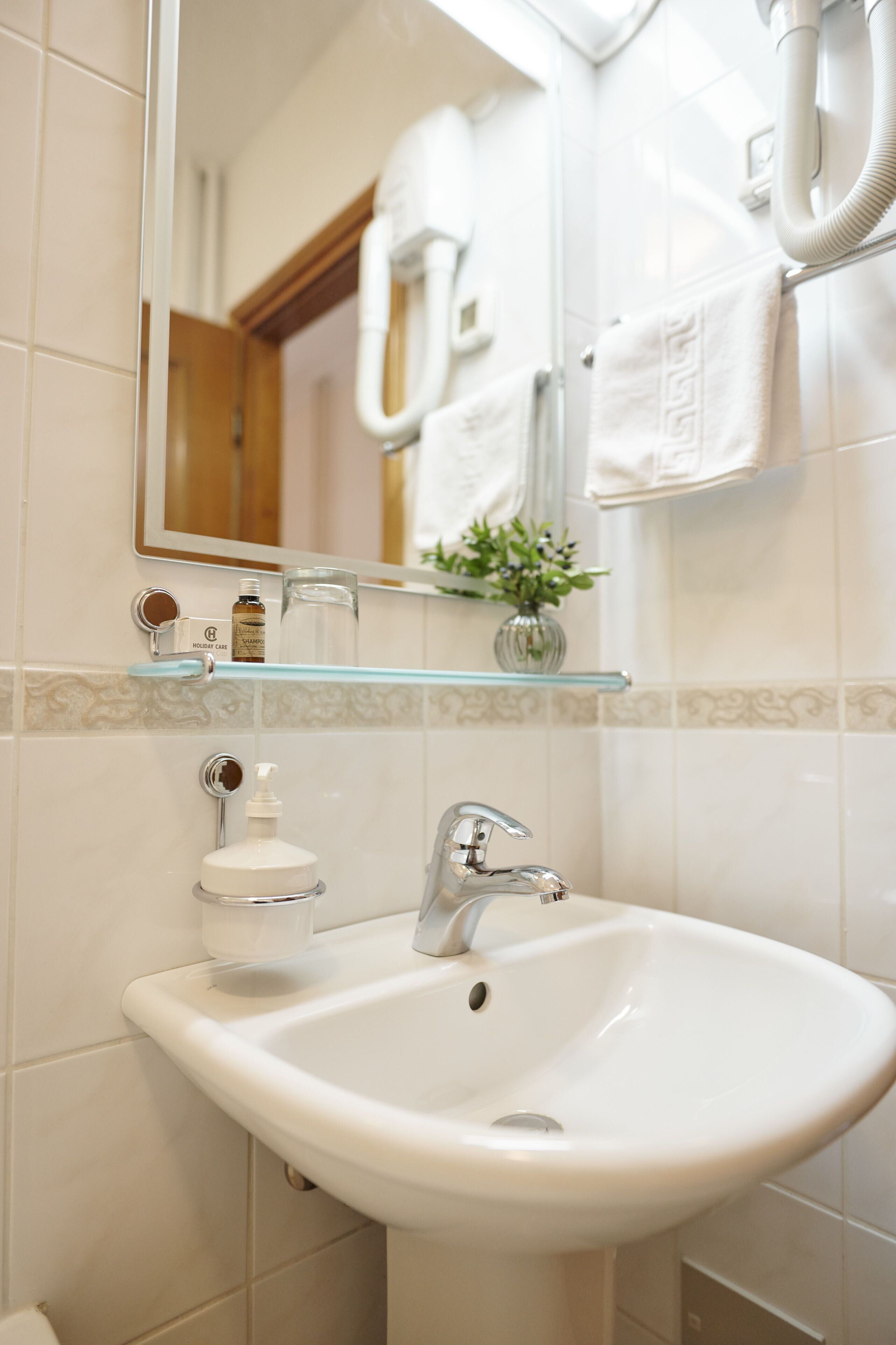 A bathroom with a white sink, a mirror, and a glass shelf holding toiletries.