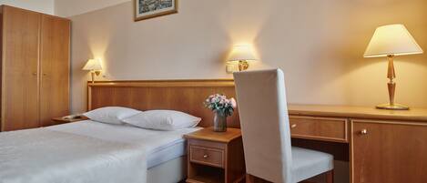 A hotel room with a bed, a desk, a chair, a nightstand, and two lamps.