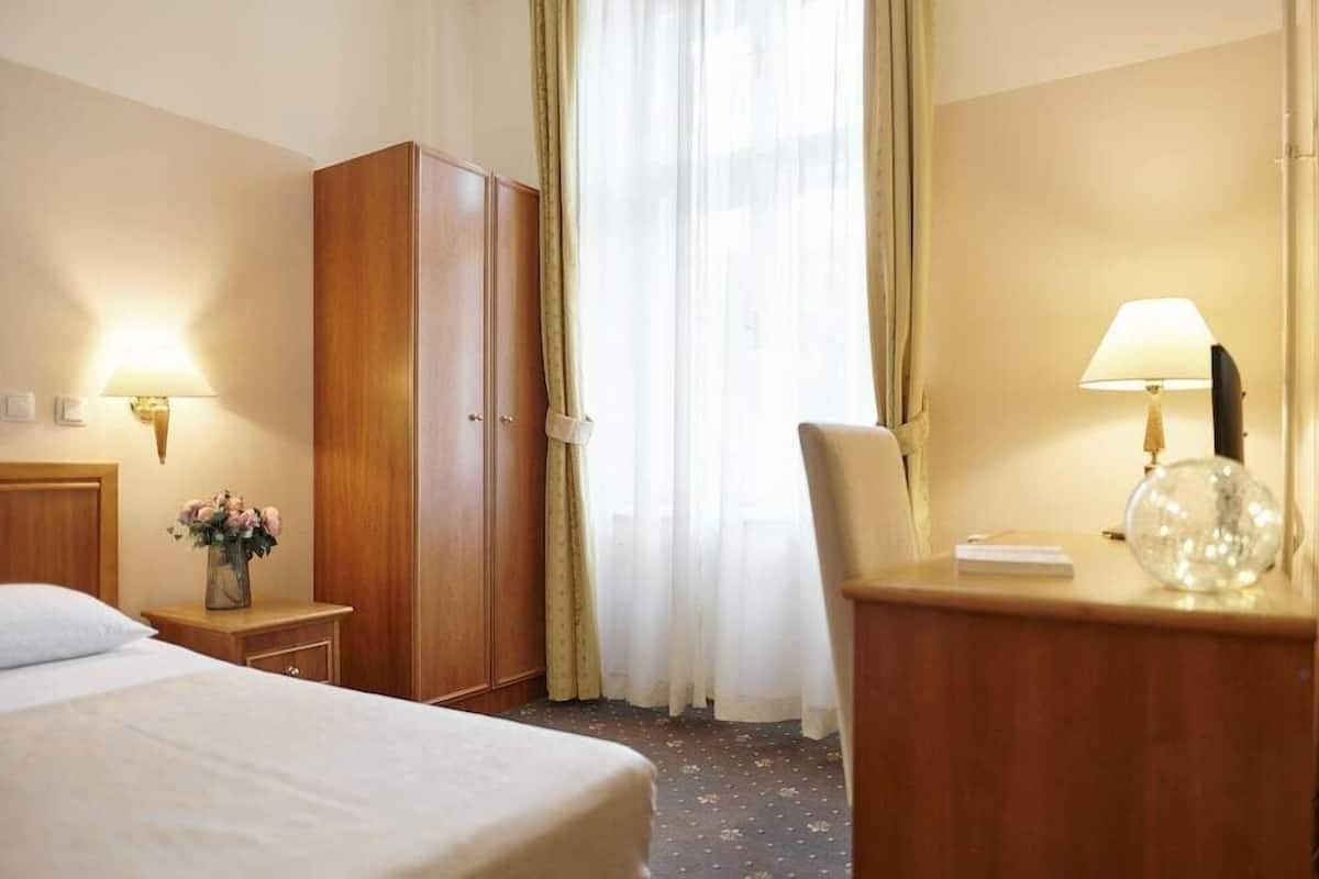 A hotel room with a bed, a wardrobe, a desk with a lamp, and a window with curtains.