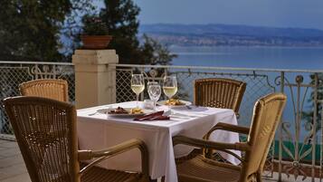 Una mesa de comedor con sillas de mimbre, mantel blanco y copas de vino, con vistas a un paisaje escénico.