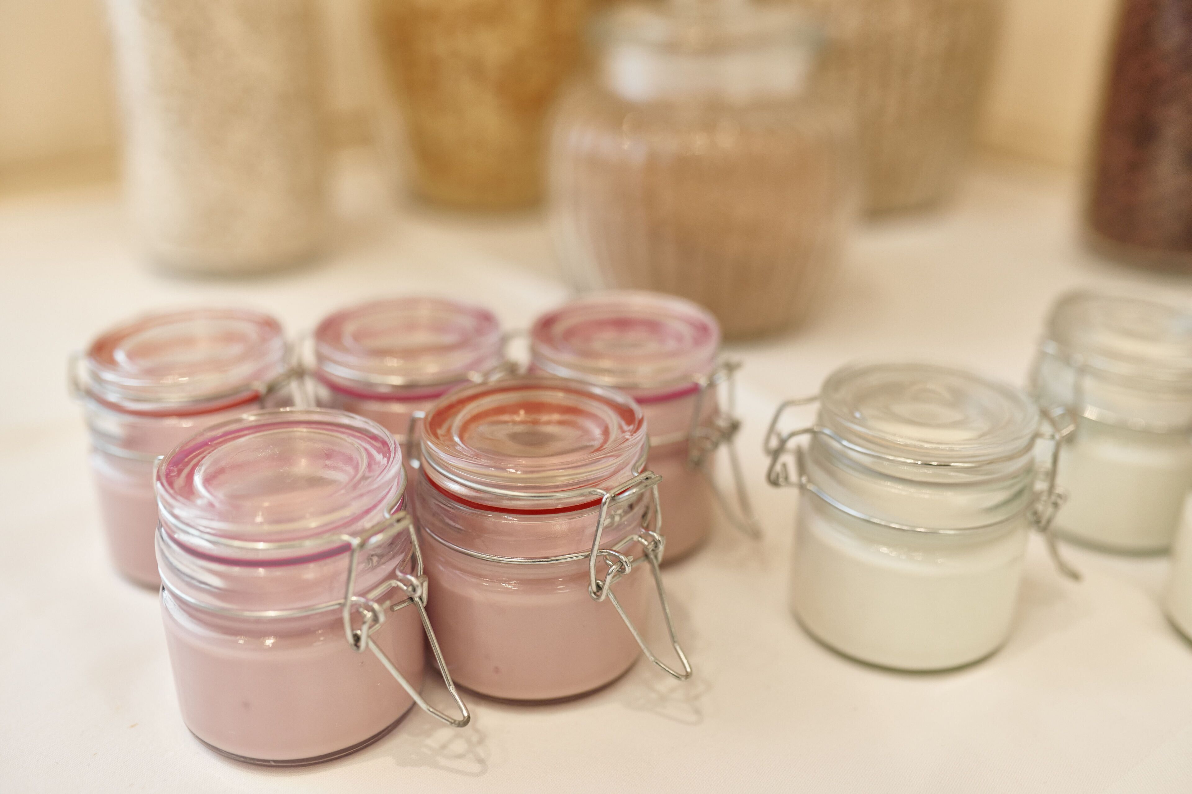 Small glass jars with metal clasps, some containing pink and white substances, arranged on a surface.