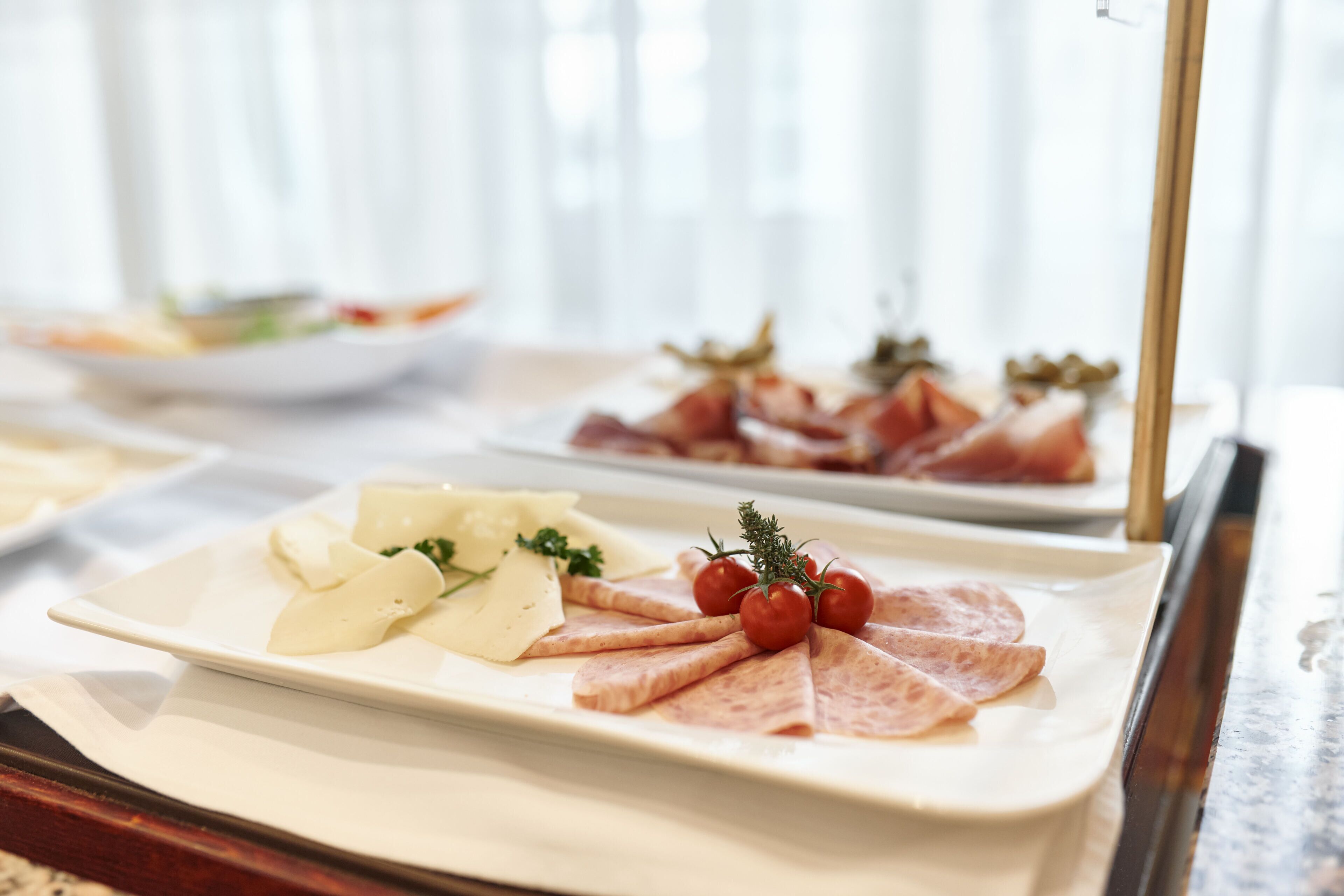 A buffet table with various food items including sliced meats, cheeses, and tomatoes.