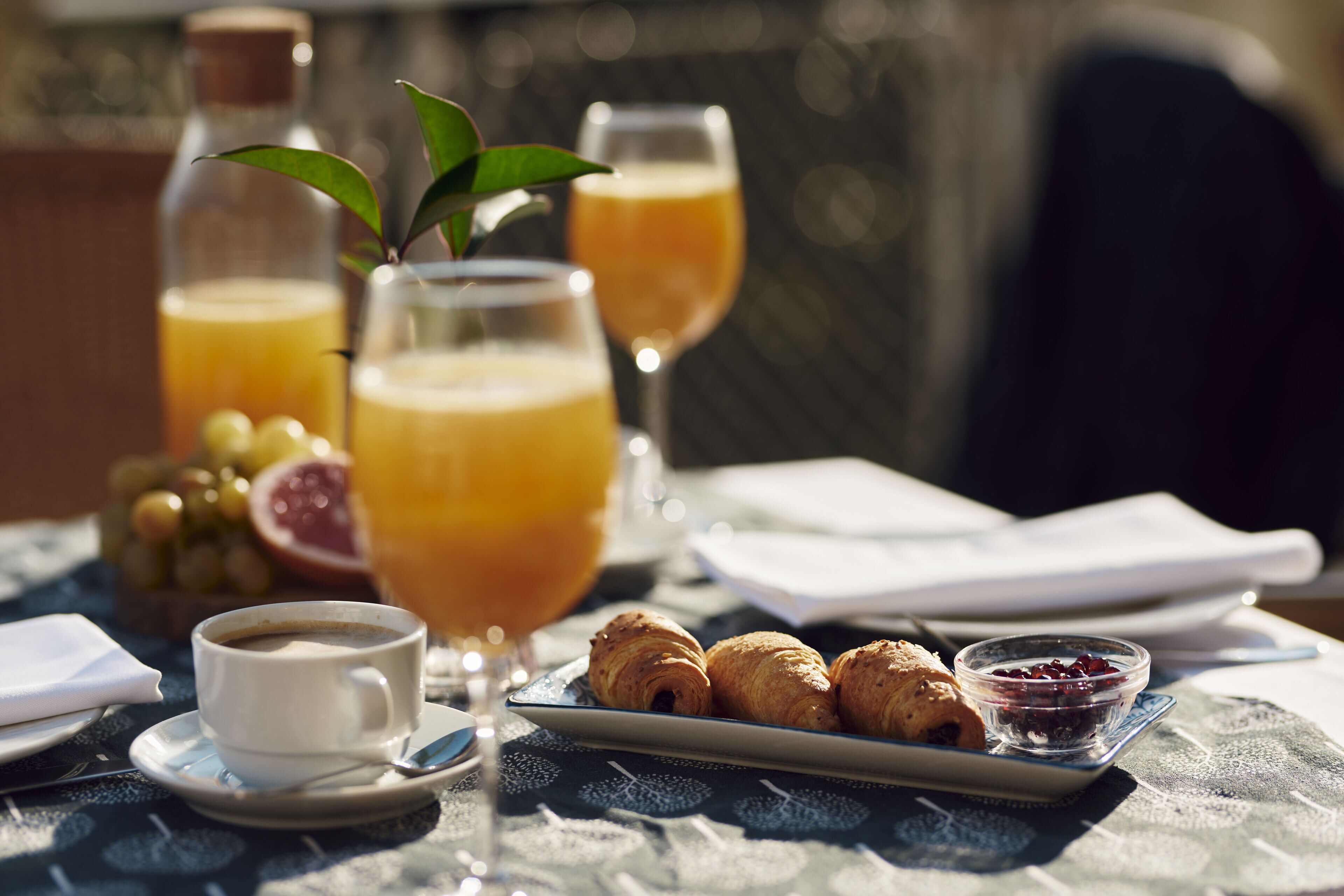 Een ontbijttafel met croissants, koffie, sinaasappelsap en een fles sap.