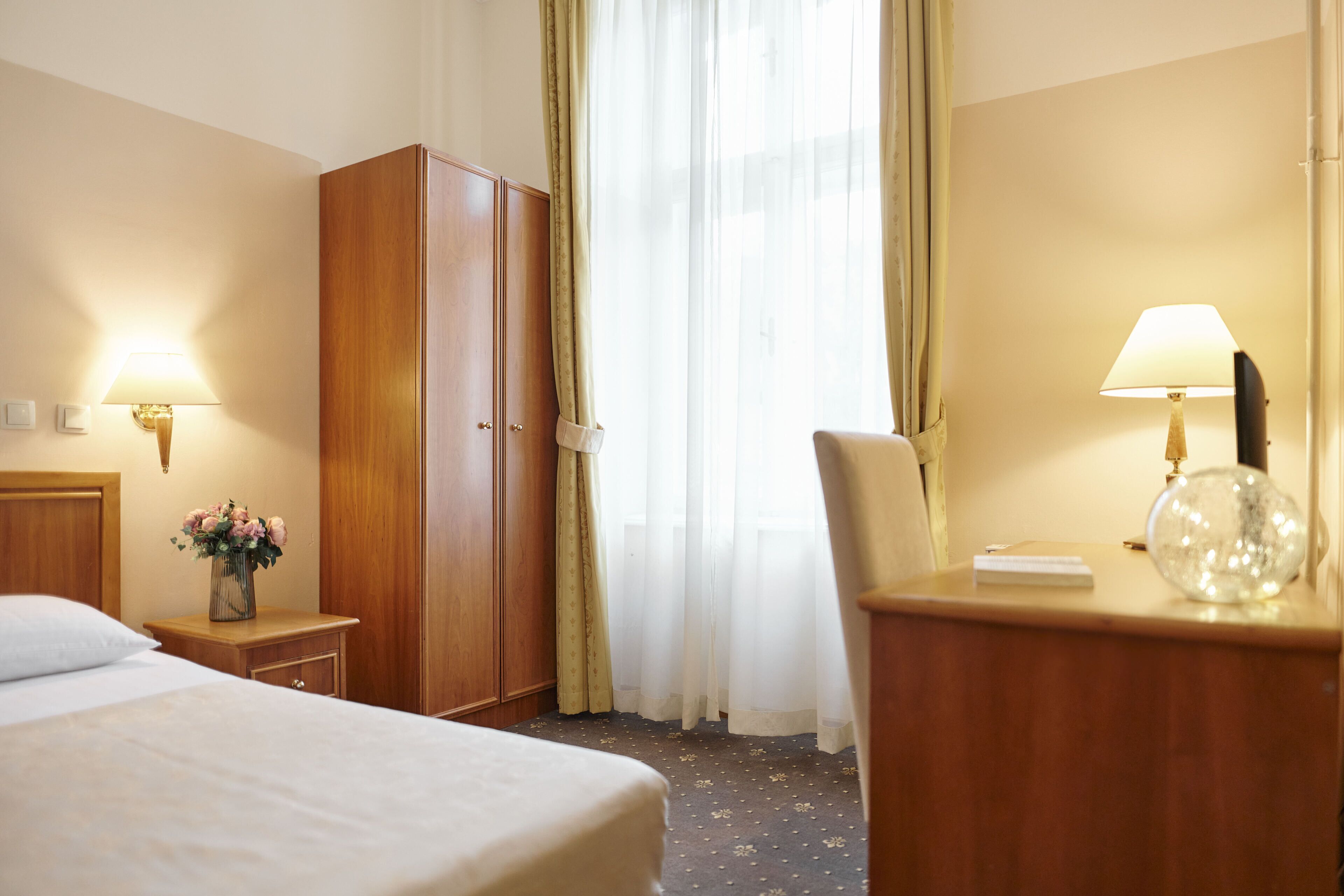 Habitación de hotel con cama, armario de madera, mesita de noche con lámpara y una silla.