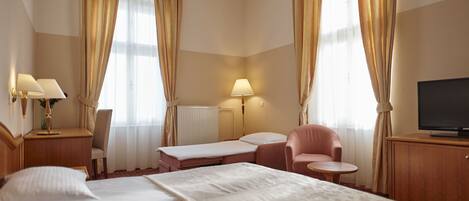 A hotel room with a large bed, two bedside tables with lamps, a desk with a chair, a small round table, and a television on a cabinet.