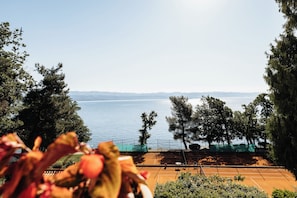 A tennis court with a view of a lake and distant mountains. - Hotel Lovran (Lovran)