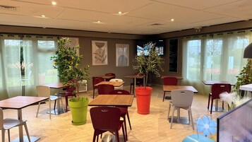 Un comedor con mesas, sillas, plantas en macetas y una pizarra con el menú.