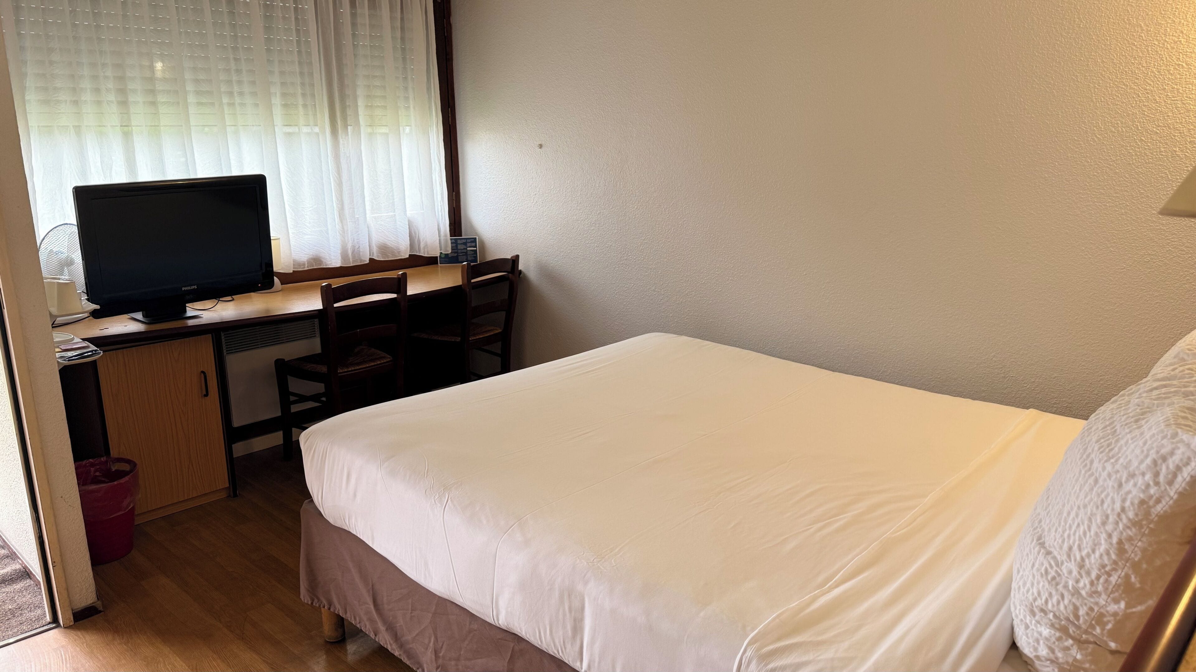 Une chambre d’hôtel avec un lit, un bureau avec un ordinateur, une chaise et une fenêtre avec des rideaux.