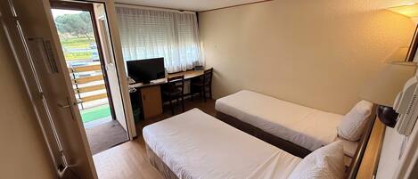 A room with two beds, a desk with a TV, and a door leading outside.