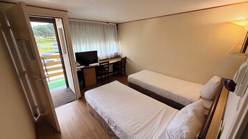 Una habitación con dos camas, un escritorio con televisor y una puerta que da al exterior.