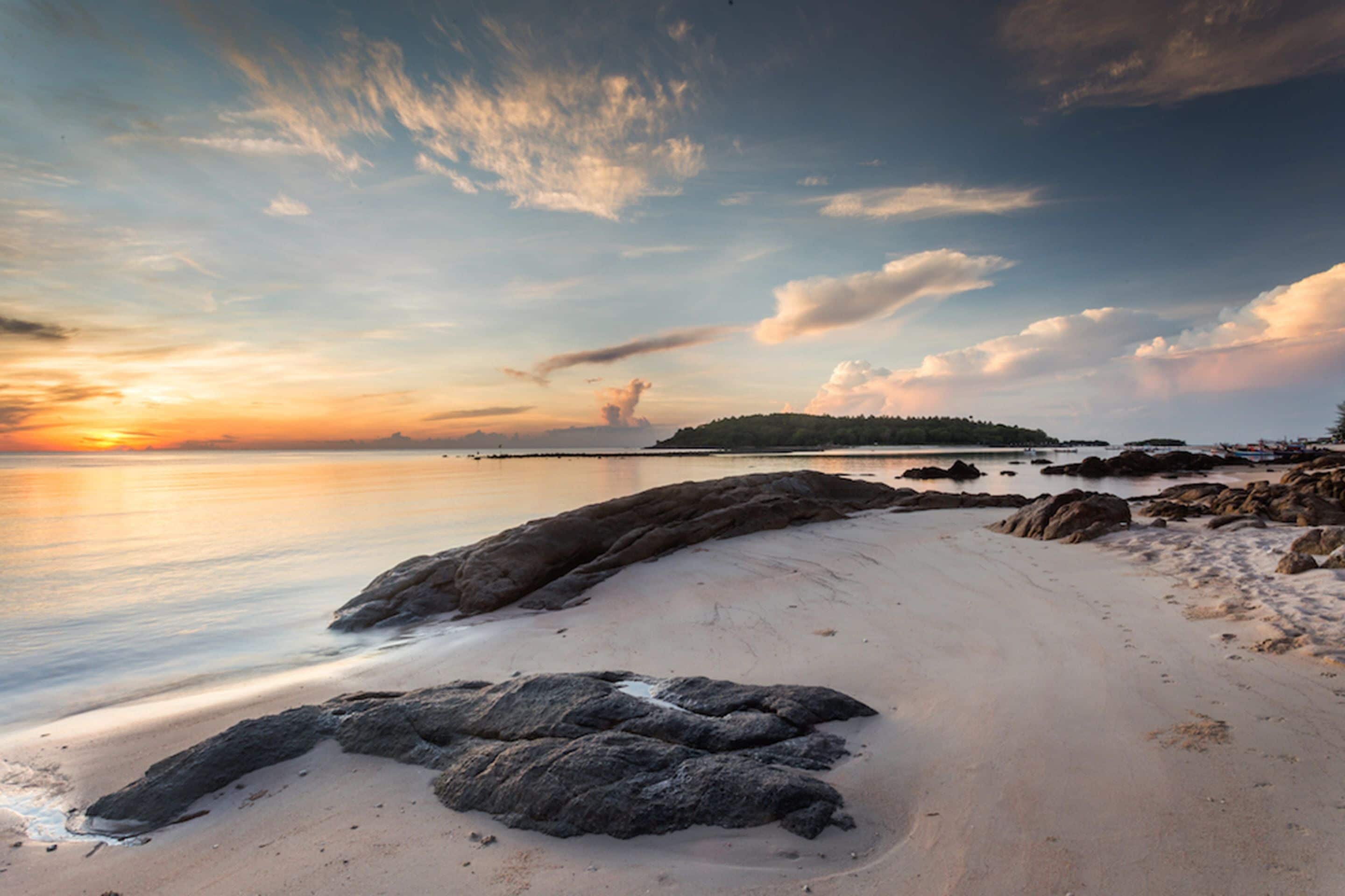 A beach with a rocky shoreline, calm water, and a distant island.