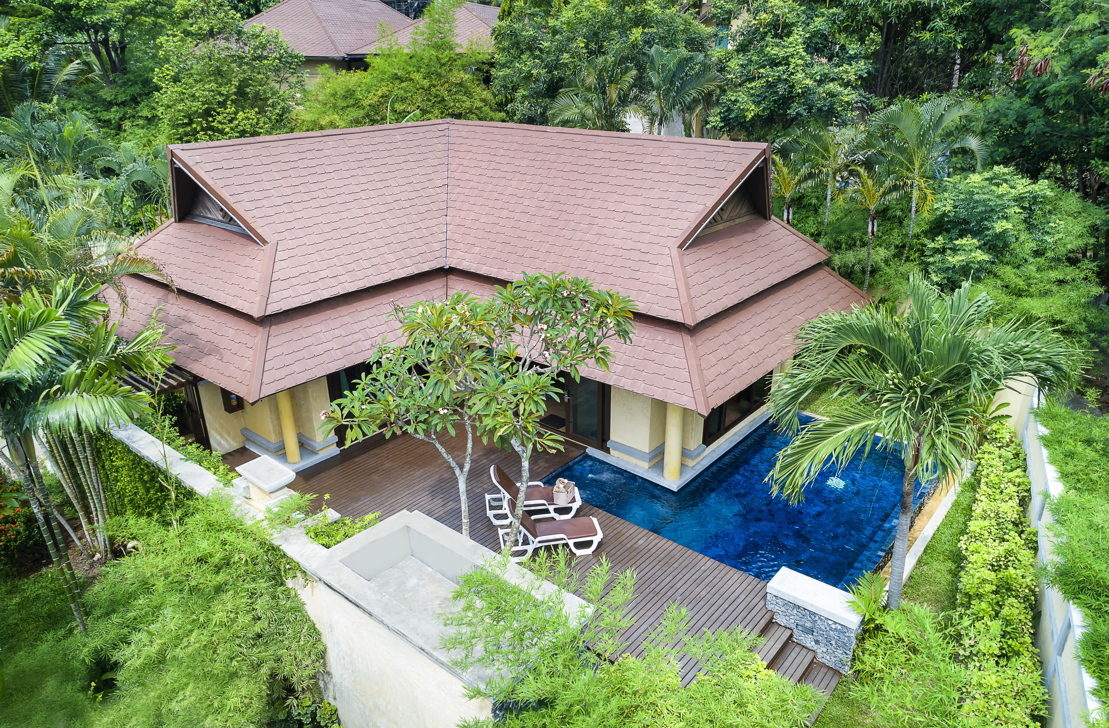 A two-story house with a swimming pool, surrounded by lush greenery and palm trees.