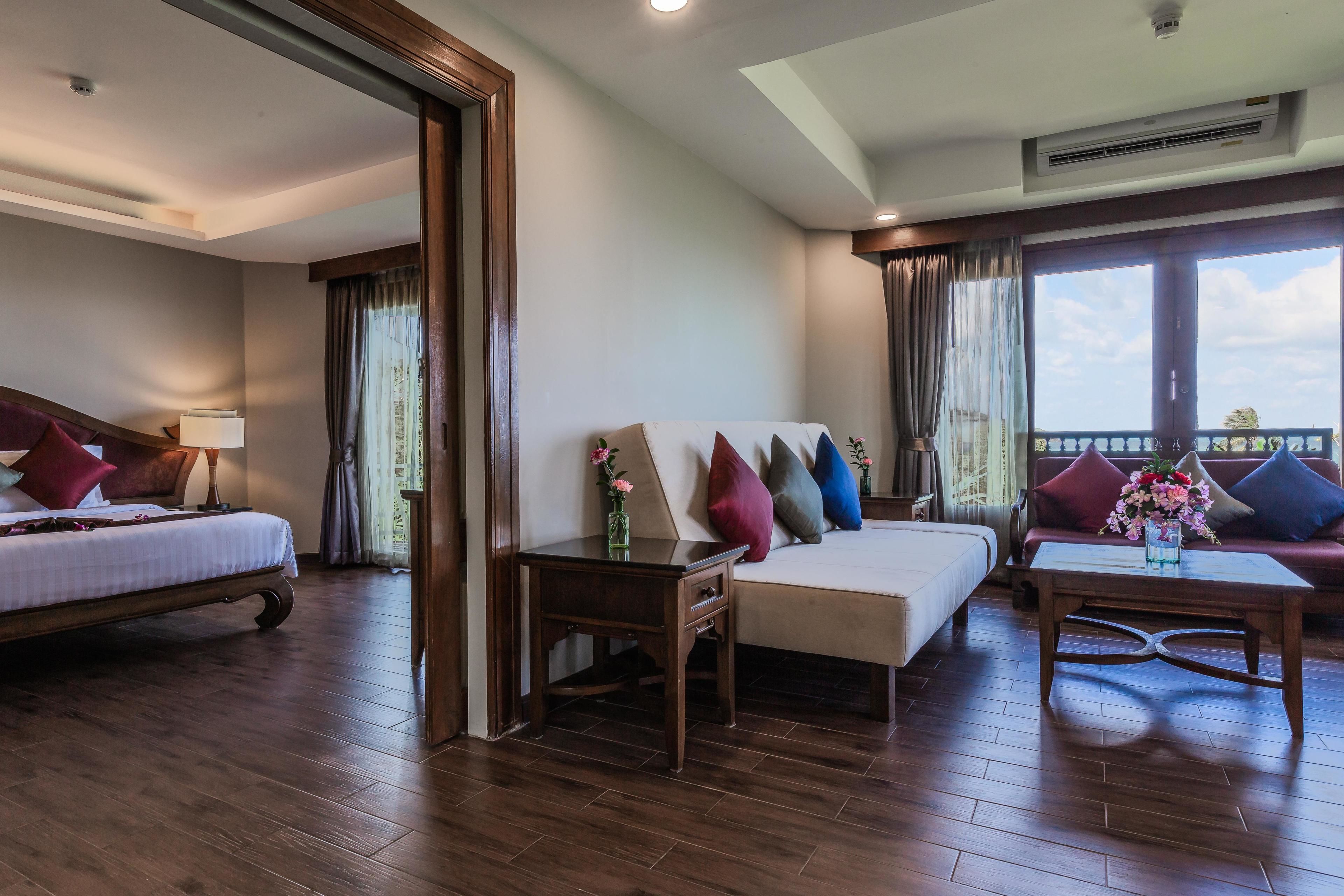A hotel room with a bed, a sofa, a coffee table, and a small table with a vase of flowers.