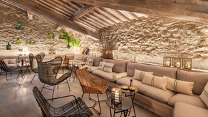 An interior with a stone wall, wooden ceiling beams, a sofa set, wicker chairs, and a small table with a candle. - Badia di Pomaio small luxury hotels of the world  (Arezzo)