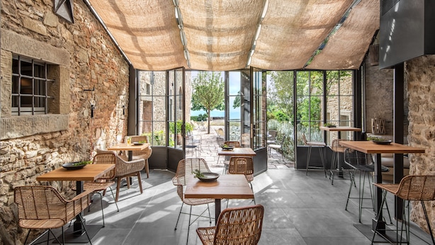 An outdoor café with stone walls, wicker furniture, and large windows offering a view of the sea. - Badia di Pomaio small luxury hotels of the world  (Arezzo)