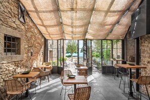An outdoor café with stone walls, wicker furniture, and large windows offering a view of the sea. - Badia di Pomaio small luxury hotels of the world  (Arezzo)