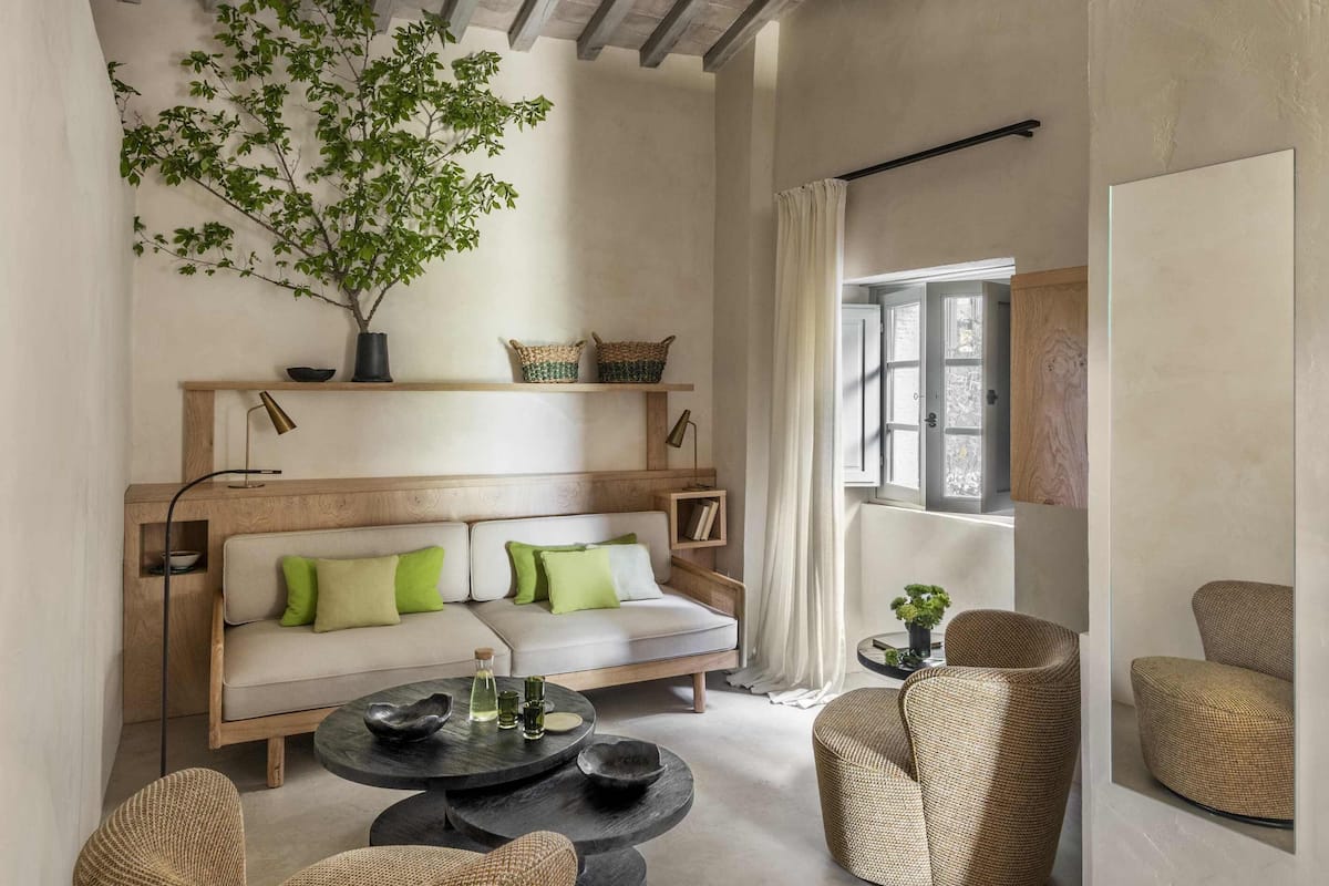 Un accogliente soggiorno con soffitto in legno, un divano con cuscini verdi, un tavolino rotondo e poltrone in vimini.