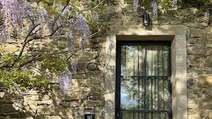 A stone building with a door and window, surrounded by greenery and a flowering tree. - Badia di Pomaio small luxury hotels of the world  (Arezzo)