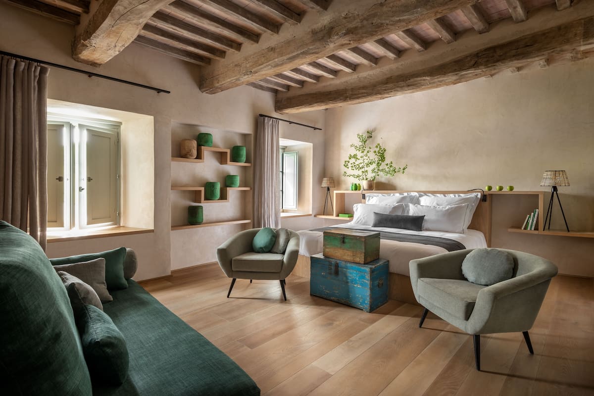Un soggiorno spazioso con soffitto in legno, un divano verde, due poltrone, un tavolino da caffè e un letto con un comodino.