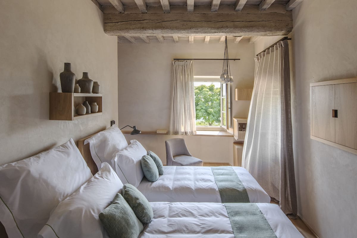 Una camera da letto con soffitto in legno, un letto con biancheria da letto bianca e dettagli verdi, un comodino con una lampada e una finestra con tende.