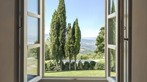 A room with a large window offering a view of trees and a distant landscape. - Badia di Pomaio small luxury hotels of the world  (Arezzo)