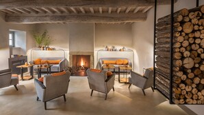 A cozy living room with a fireplace, comfortable seating, and a log wall. - Badia di Pomaio small luxury hotels of the world  (Arezzo)