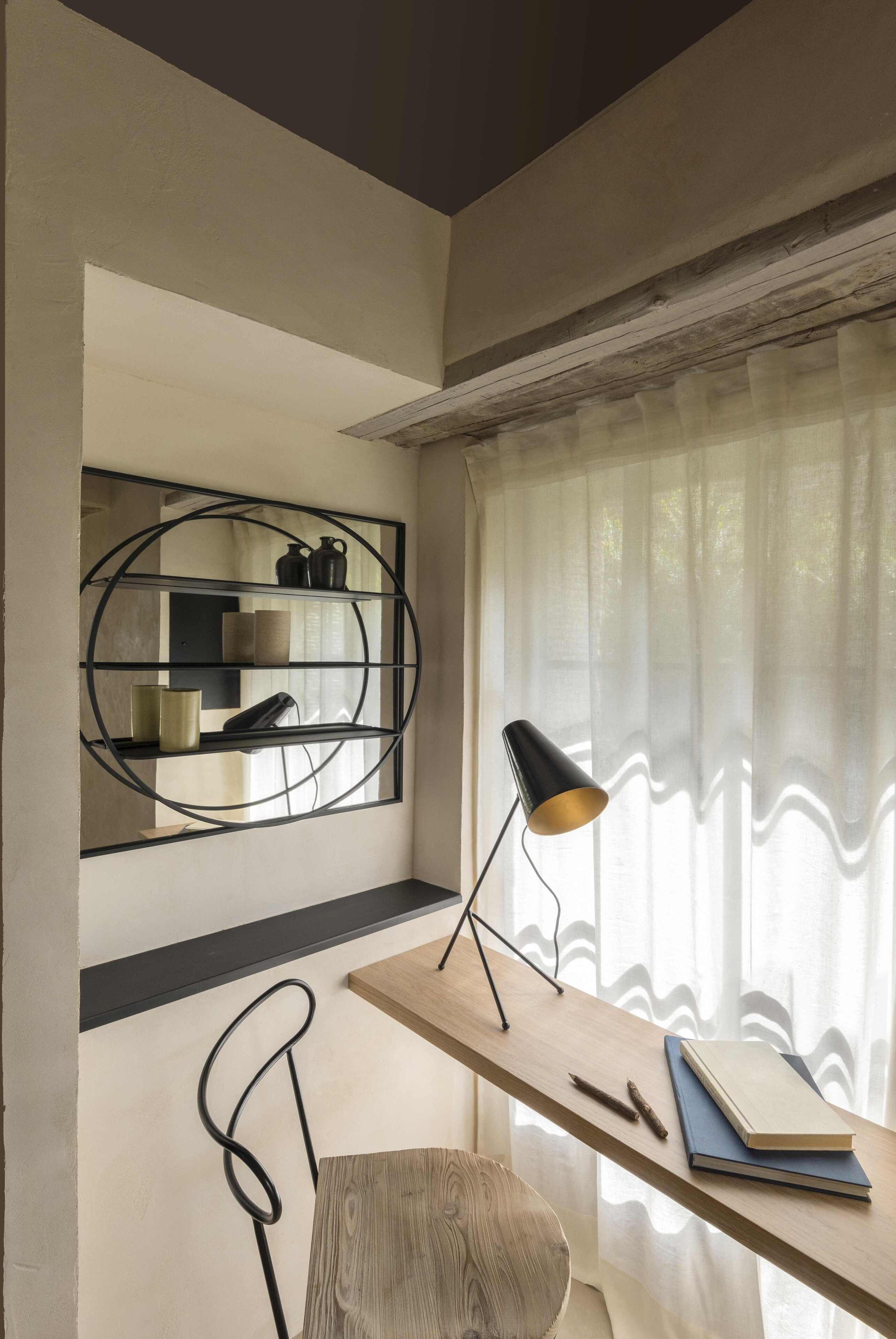 A modern room with a wooden desk, a black lamp, a chair, and a wall-mounted shelf with decorative items.