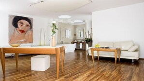 Una sala moderna con suelo de madera, un sofá blanco, una mesa de comedor con un bol y un cuadro en la pared.