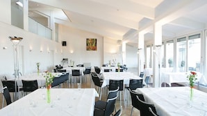 Un amplio comedor con varias mesas dispuestas para recibir a los huéspedes, con sillas modernas y manteles blancos.